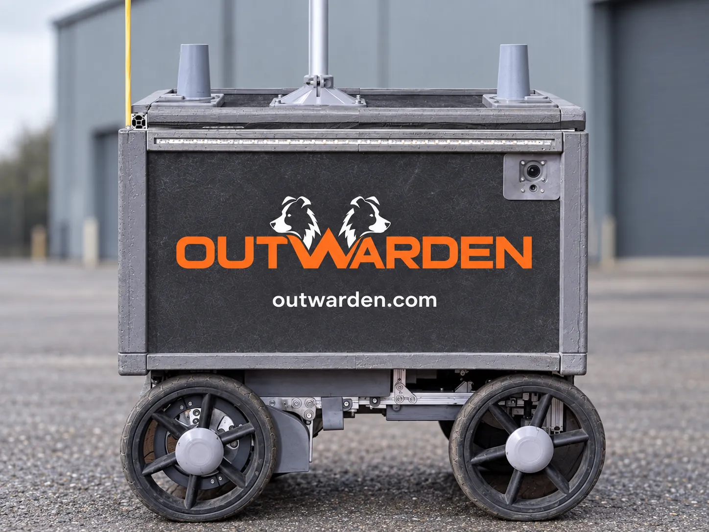 Side view of the Outwarden security robot on yard tarmac, showing its branded panel, body camera, LED strip and wheels